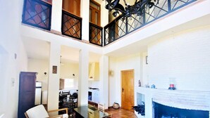 A spacious living area with a dining table, chairs, a fireplace, and a kitchen in the background.