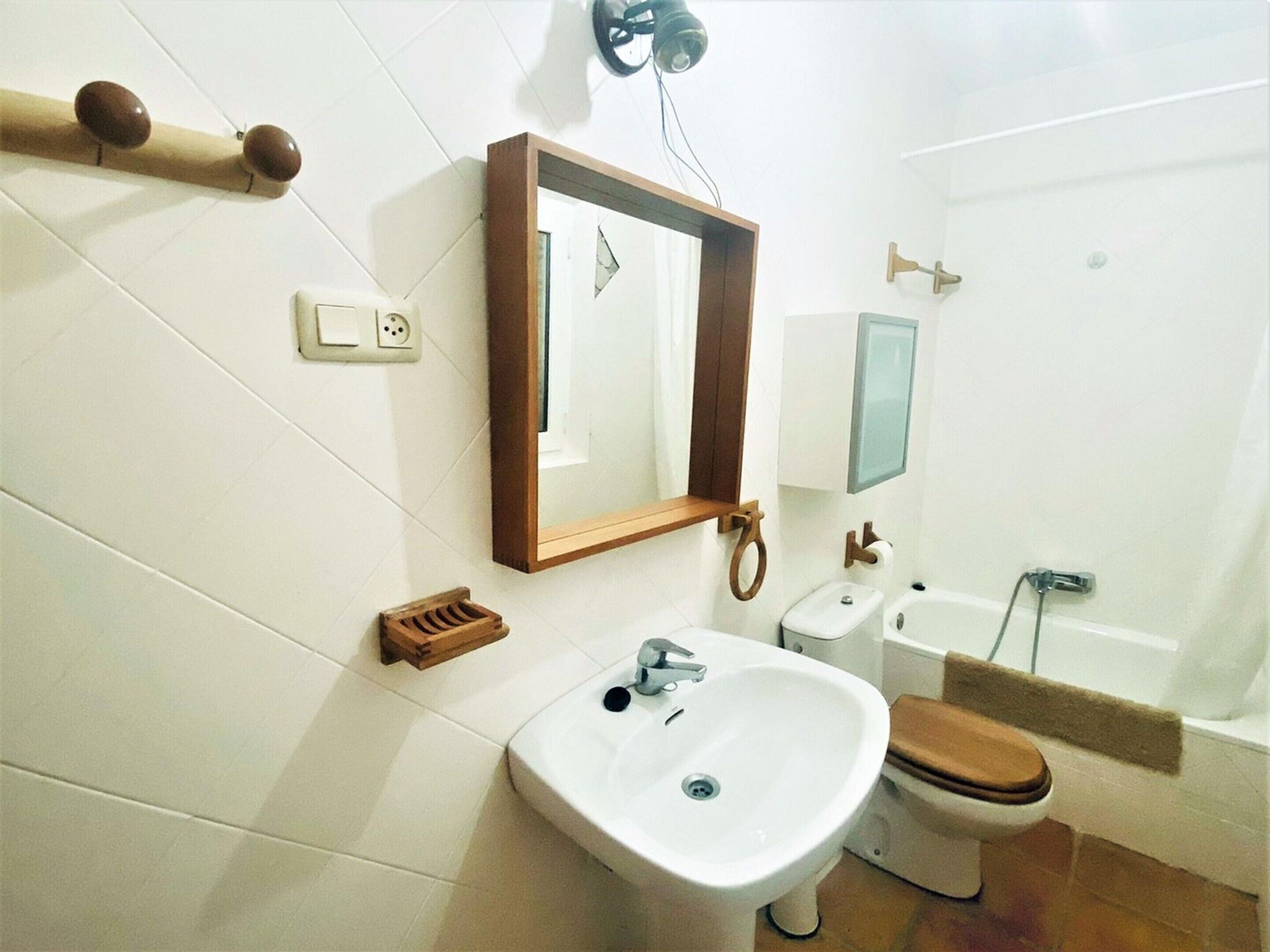 A bathroom with a sink, toilet, and bathtub. There is a mirror above the sink and a towel rack on the wall.