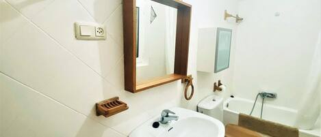 A bathroom with a sink, toilet, and bathtub. There is a mirror above the sink and a towel rack on the wall.