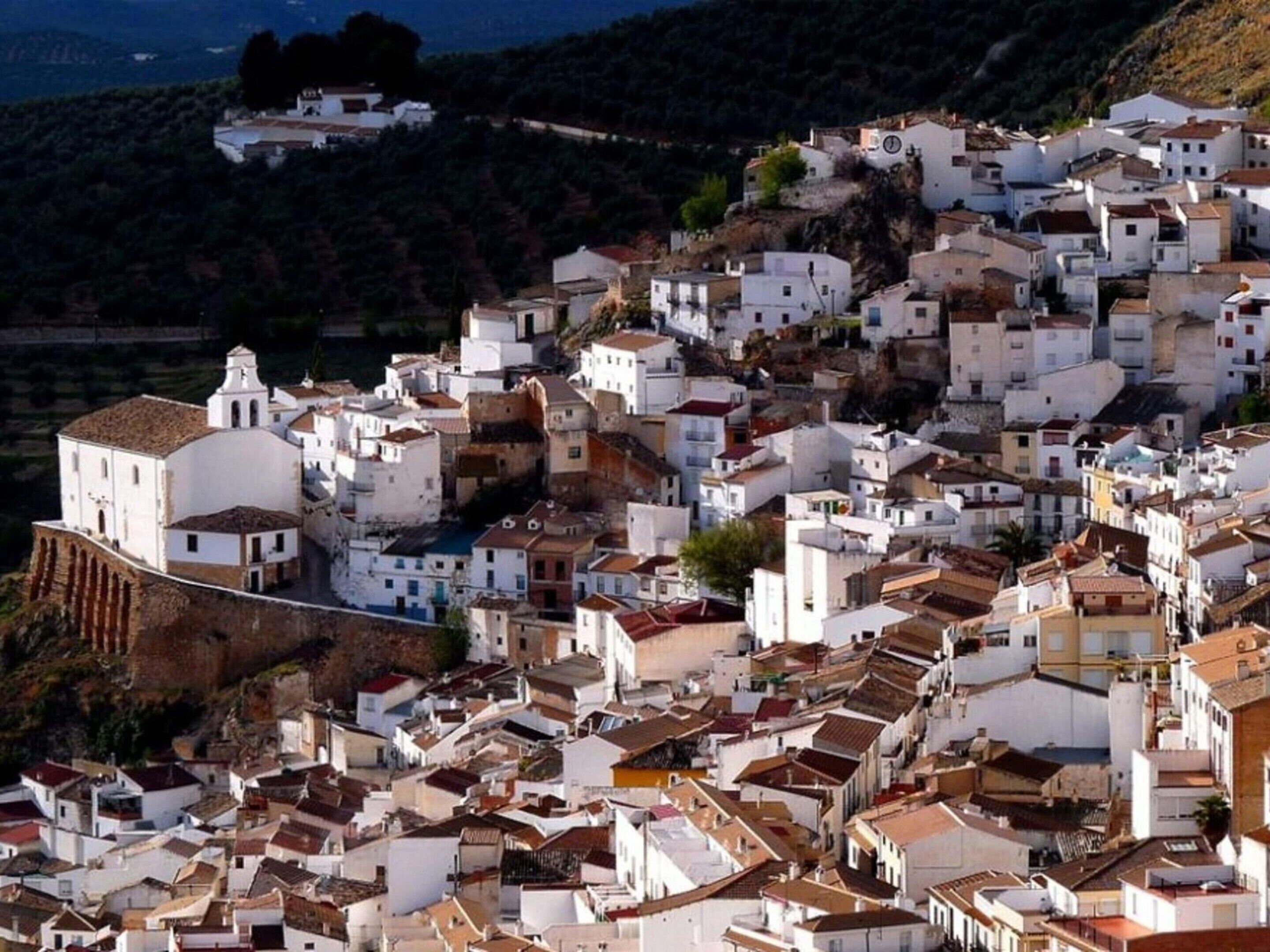 A densely packed hillside town with white buildings, some with domed roofs, and a prominent church with a bell tower.