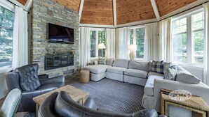 A cozy living room with a stone fireplace, leather sofas, and large windows. - 7 bed, 5 bath spectacular cottage on Lake Joseph! (Parry Sound Mid-Shore (Bala))