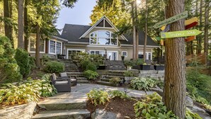 A two-story house with a stone staircase leading to a front porch, surrounded by lush greenery and a large tree with directional signs. - 7 bed, 5 bath spectacular cottage on Lake Joseph! (Parry Sound Mid-Shore (Bala))