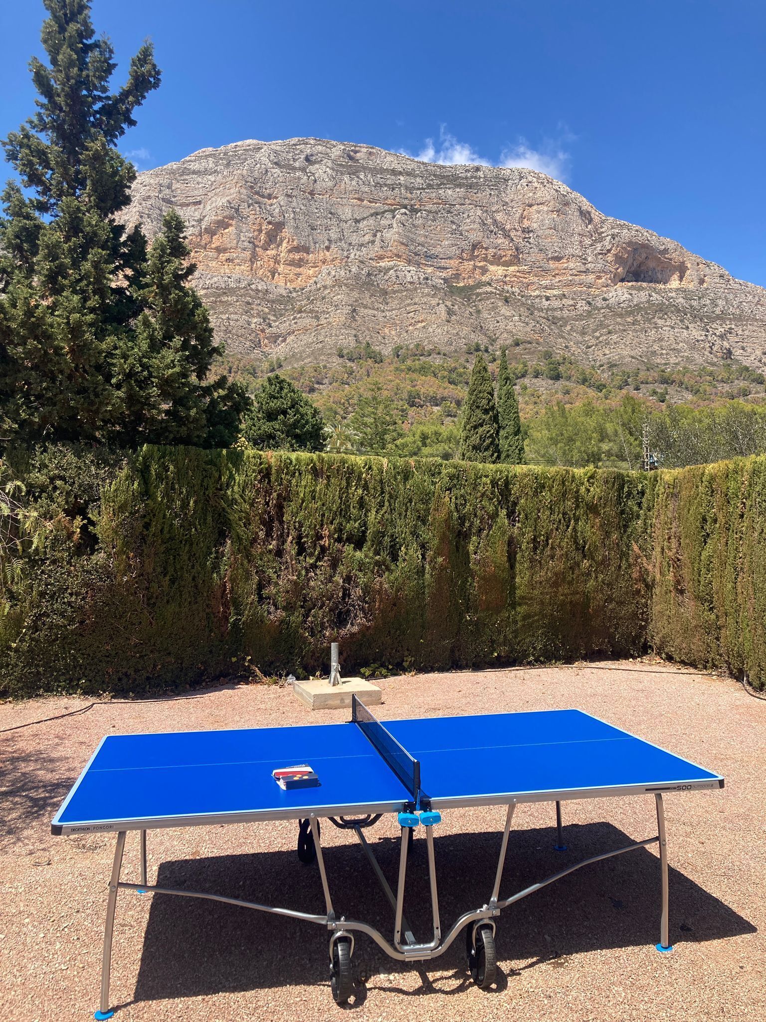A ping pong table in an outdoor area with a mountain in the background.