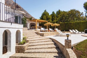 A stone staircase leading to a covered outdoor seating area with lounge chairs and umbrellas.