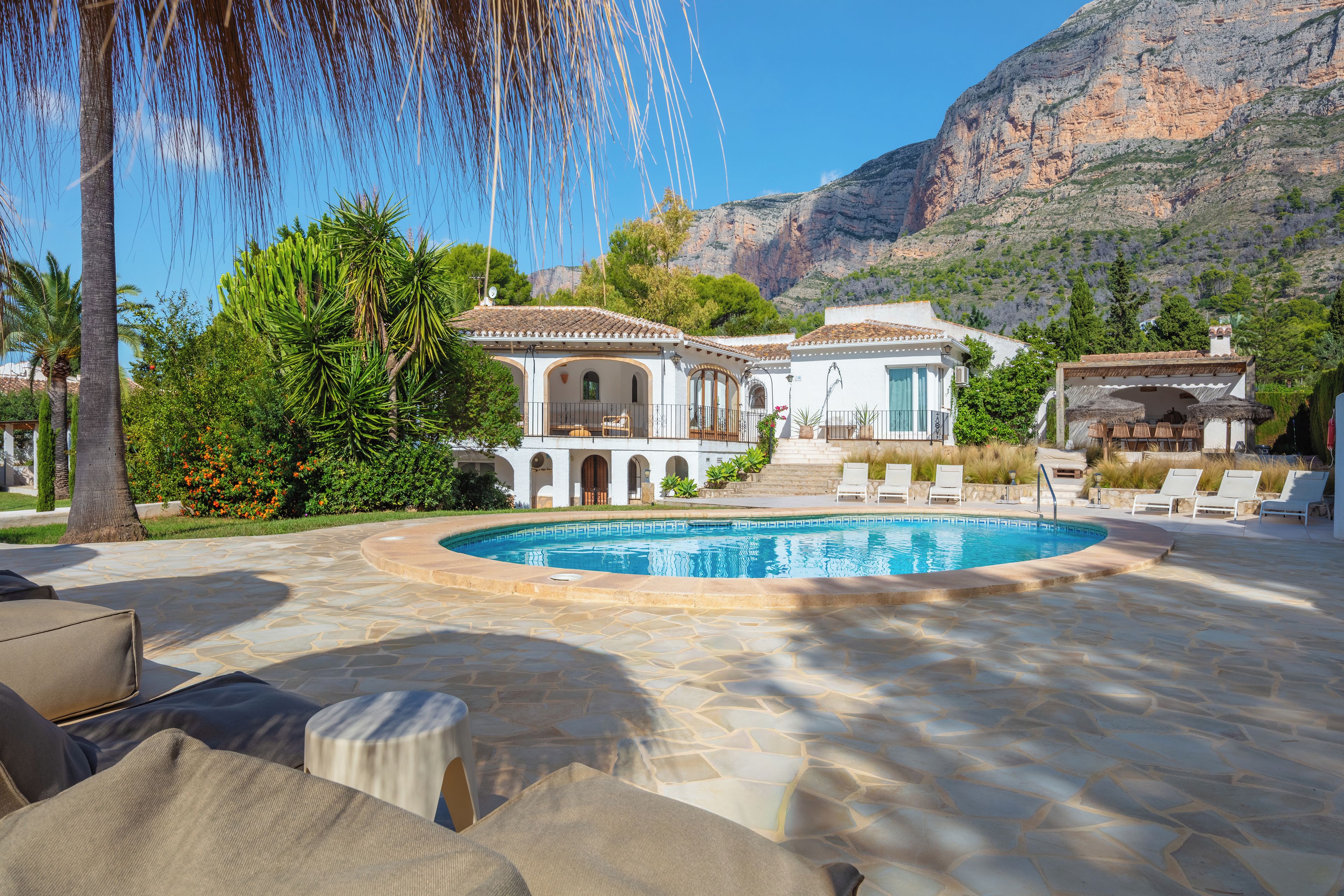 A pool area with lounge chairs and a building with a tiled roof.