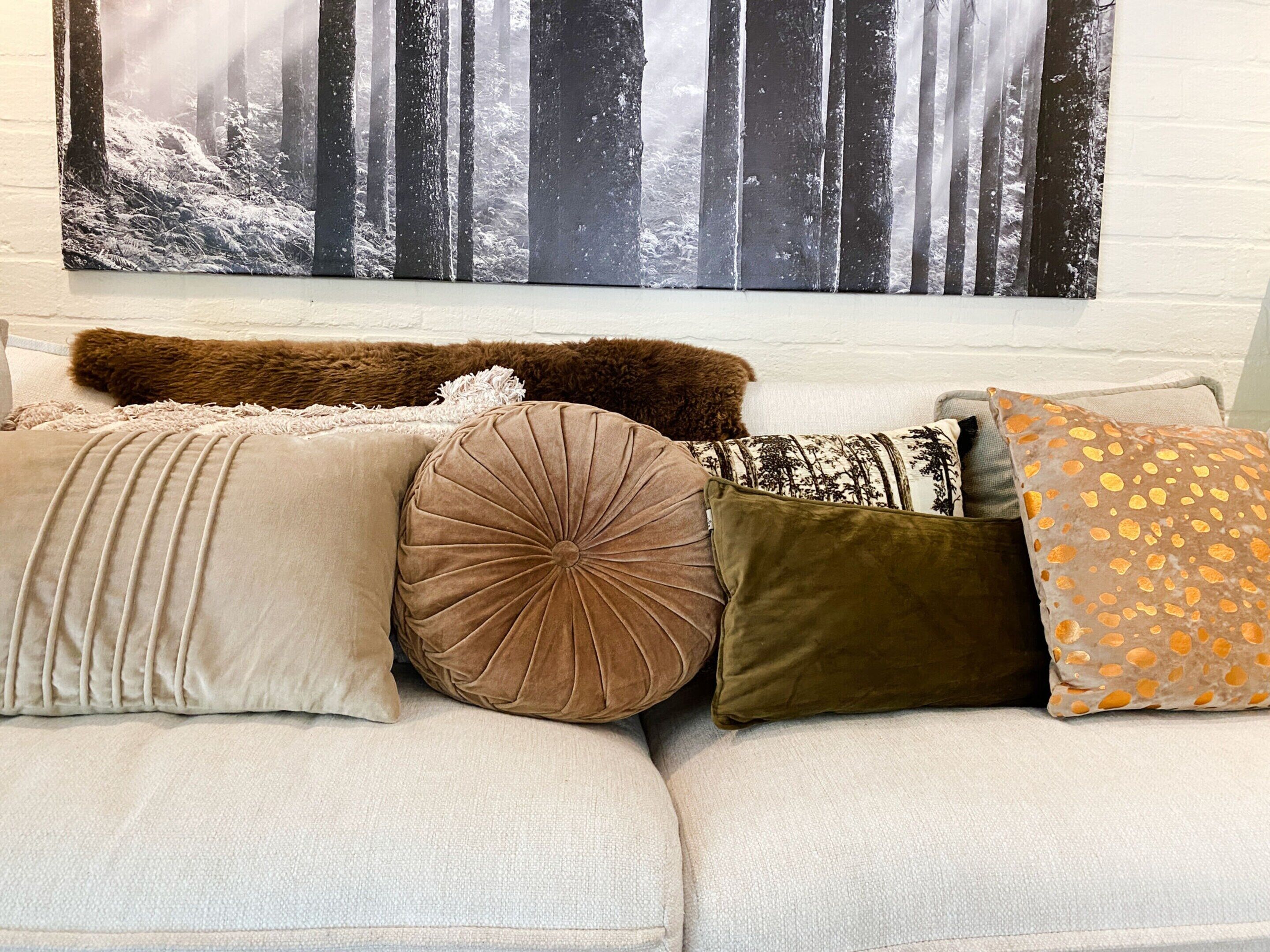 A sofa with various cushions and a forest-themed wall hanging.