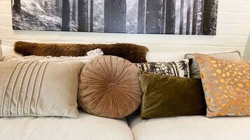A sofa with various cushions and a forest-themed wall hanging.