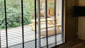 Una habitación con un ventanal grande con persianas horizontales, suelo de madera y televisor montado en la pared.