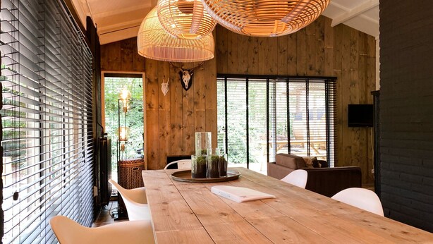 Un comedor moderno con una mesa de madera, sillas blancas y un amplio ventanal con persianas.