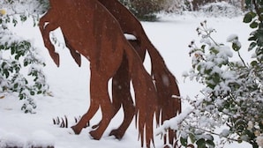 Una casa de ladrillo con tejado nevado y una escultura de metal de un caballo en primer plano.