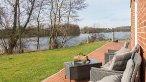 Un patio con mobiliario de mimbre, piso de ladrillo y vista a un lago.