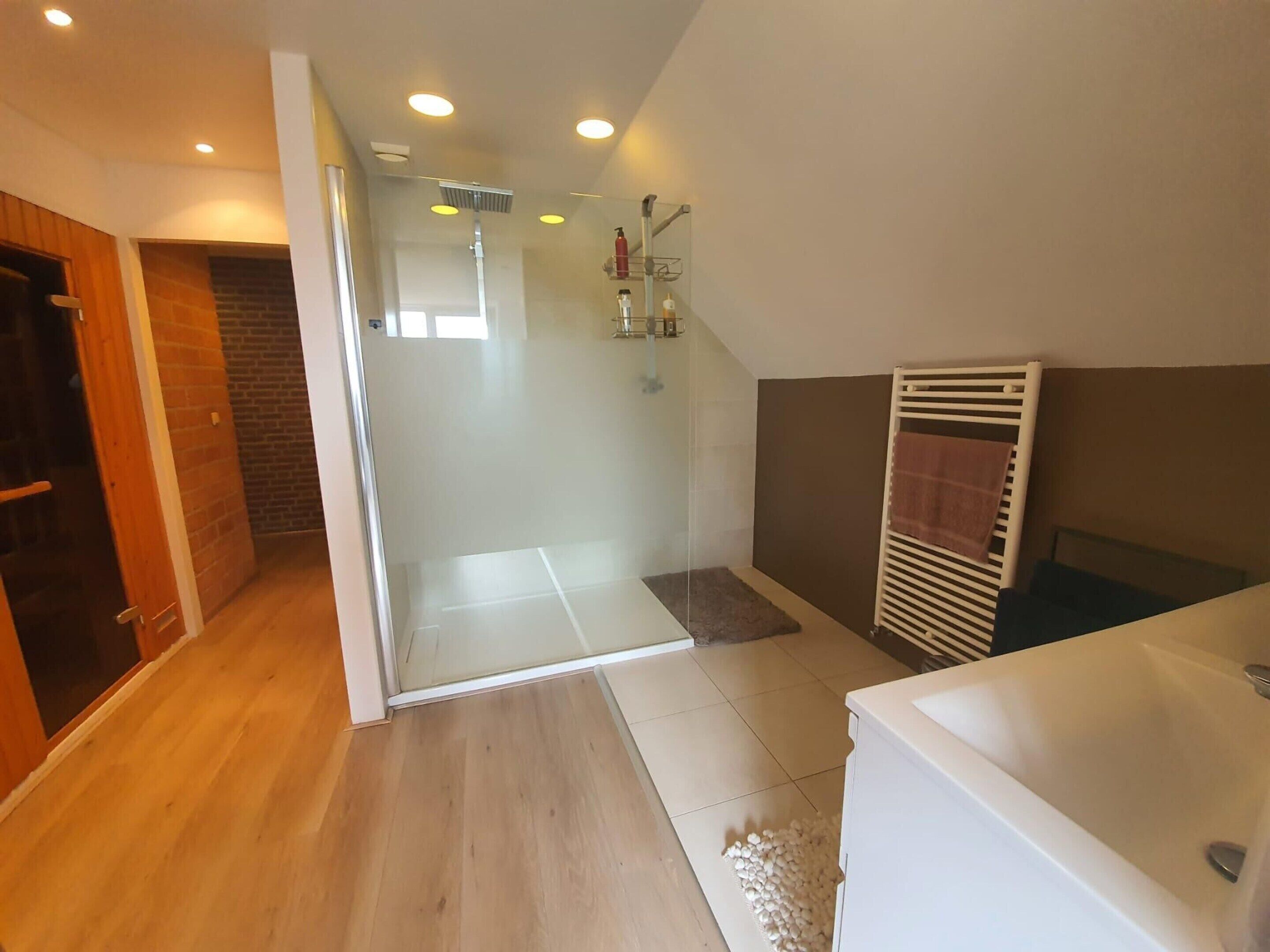 Un baño moderno con cabina de ducha de vidrio, una bañera blanca y suelo de madera.