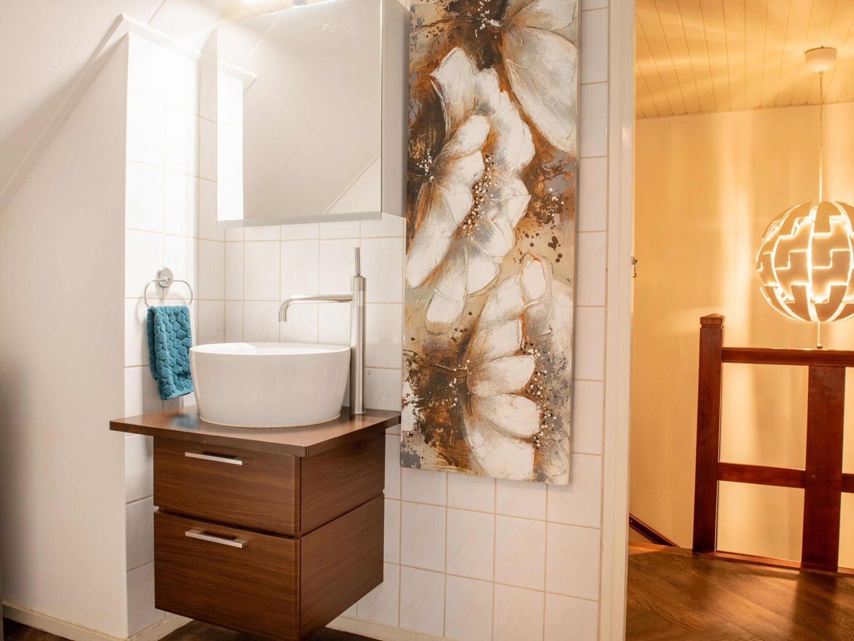A modern bathroom with a white sink, wooden vanity, and a large abstract painting.