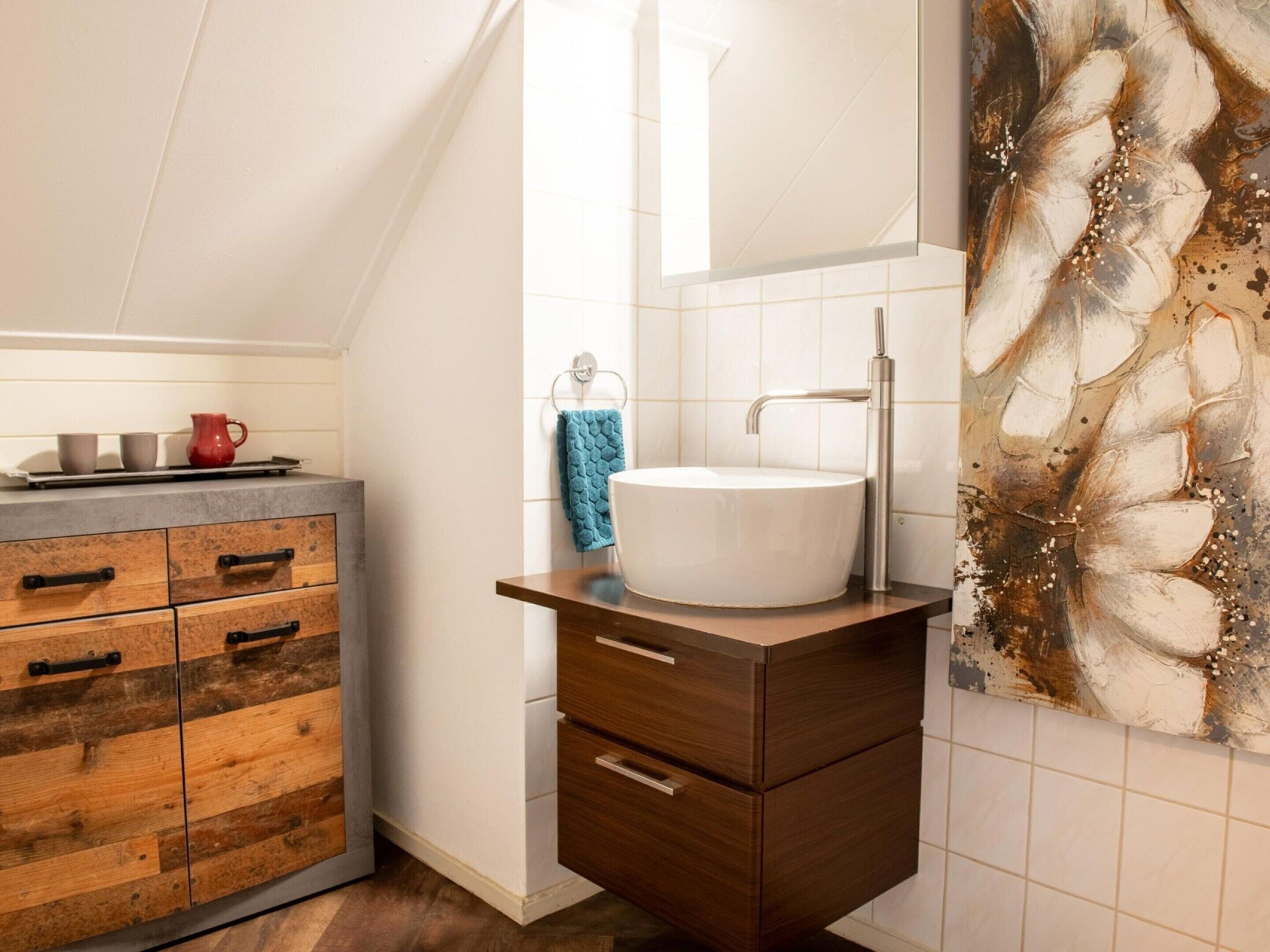 A modern bathroom with a wooden vanity, a white sink, and a large mirror.