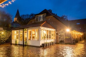 A cozy, well-lit building with a brick facade, large windows, and a small porch area with potted plants. - Farm Stay Near Bronkhorst (Steenderen)