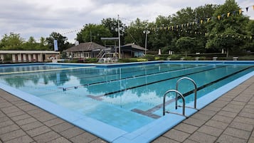 Swimmers can enjoy a refreshing dip in the pool surrounded by lush greenery and a paved walkway.