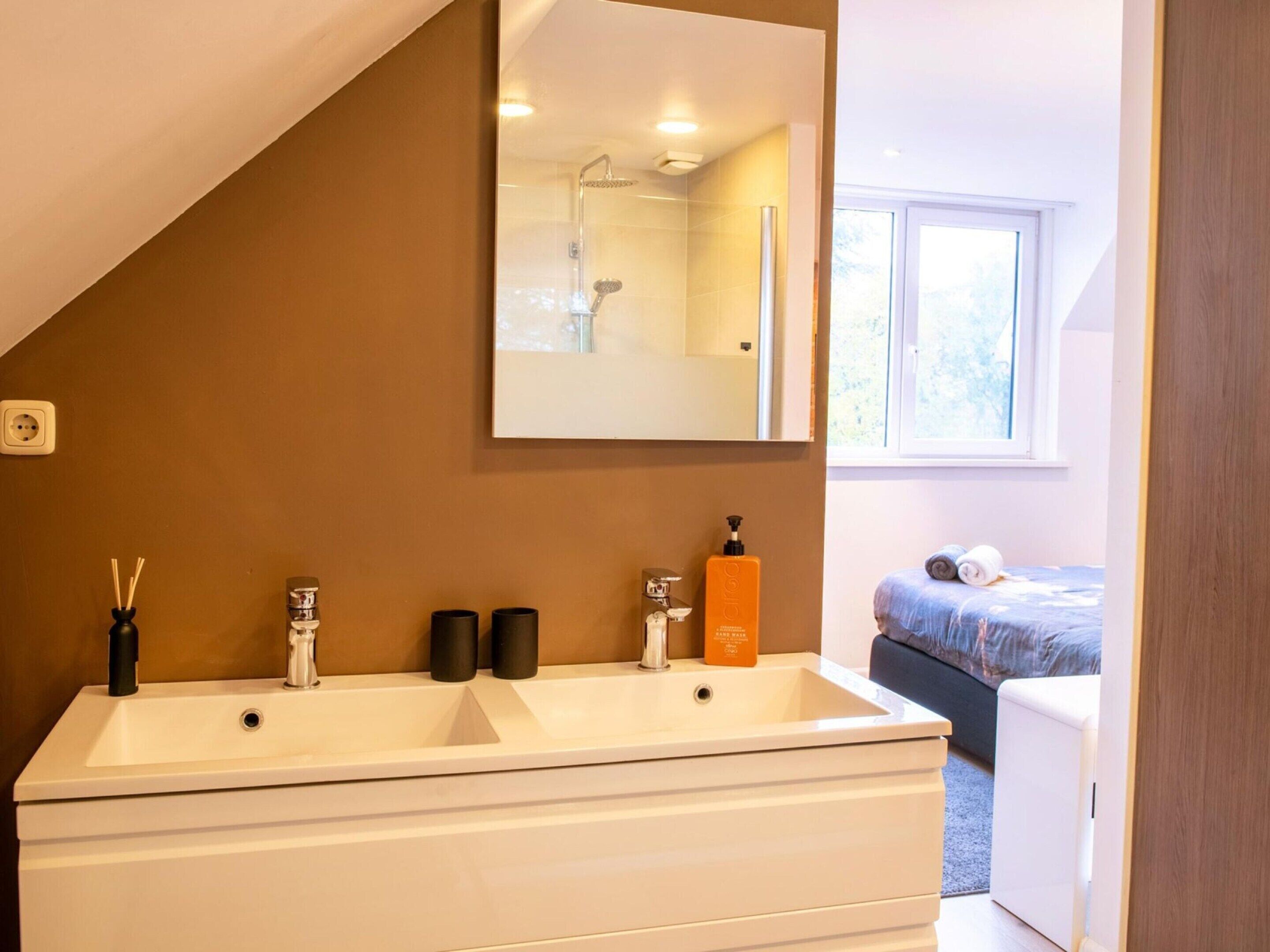 A modern bathroom with a double sink, a mirror, and a shower.