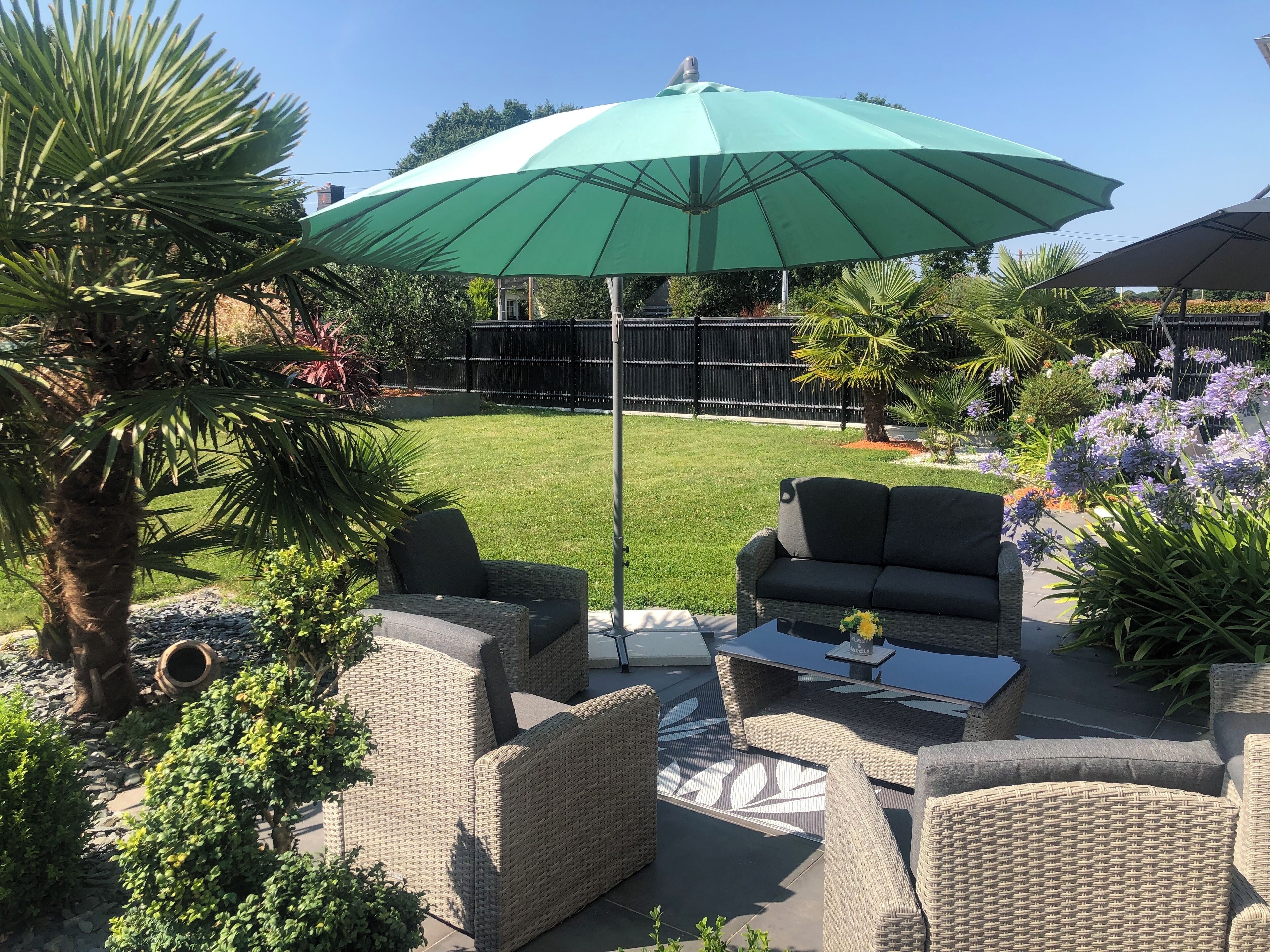 A patio area with wicker furniture, a green umbrella, and a well-maintained lawn.