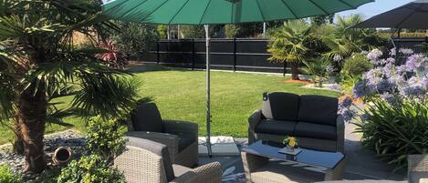 A patio area with wicker furniture, a green umbrella, and a well-maintained lawn.