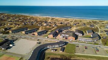 An aerial view of a coastal area with buildings, a tennis court, and a beach.