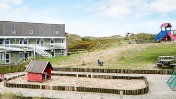 A beachside building with a sandy play area, a red structure, and a playground with slides.