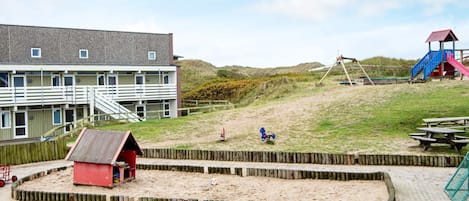 Un edificio frente a la playa con un área de juegos en la arena, una estructura roja y un parque infantil con toboganes.