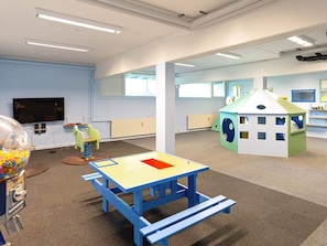 Een kinderspeelruimte met een tafel, een knutselhuisje en speelgoed.