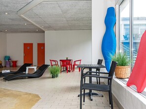 A lounge area with a tiled floor, a table with chairs, a large blue sculpture, and a window with a view of the city. - 4 Person Holiday Park Home in Ringkobing (Ringkobing)