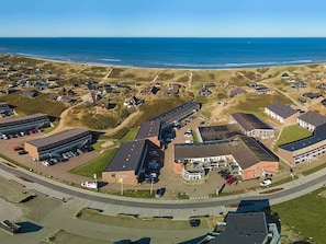 Vue aérienne d’une ville côtière, avec un mélange de bâtiments résidentiels et commerciaux, dont un grand parking et un bâtiment imposant portant une enseigne indiquant « Oceanview ».