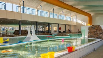 Una amplia piscina interior con diseño moderno, que incluye un elemento de onda blanca y una pared de piedra.