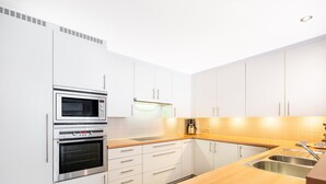 A modern kitchen with white cabinets, stainless steel appliances, a wooden countertop, and a built-in oven. - Apartment in Belgium 100m From the Sea (Koksijde)
