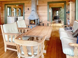 A cozy cabin interior with a central wooden table, striped chairs, a sofa, and a wood-burning stove.