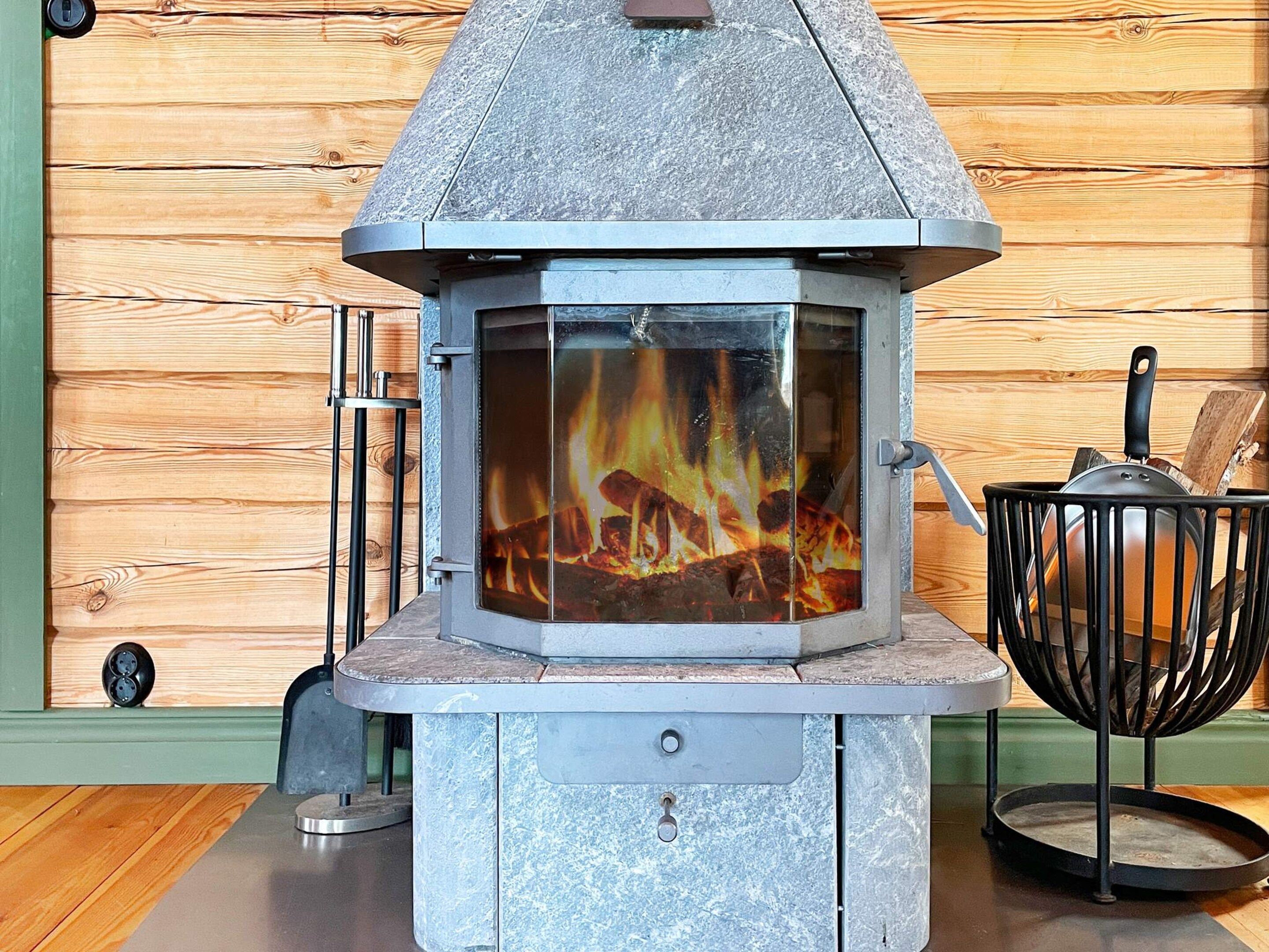 Lareira a lenha com porta de vidro, grade de metal e puxador.