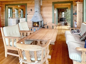 Ein gemütliches Blockhaus-Interieur mit einem zentralen Holztisch, gestreifte Polstersessel, einer Couch mit gemusterten Kissen und einem Holzofen.