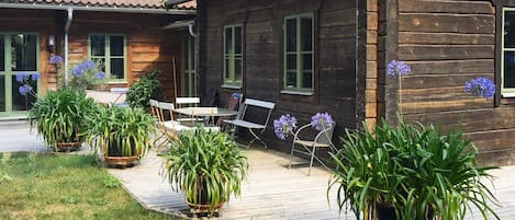 A wooden cabin with a tiled roof, outdoor seating, and potted plants.