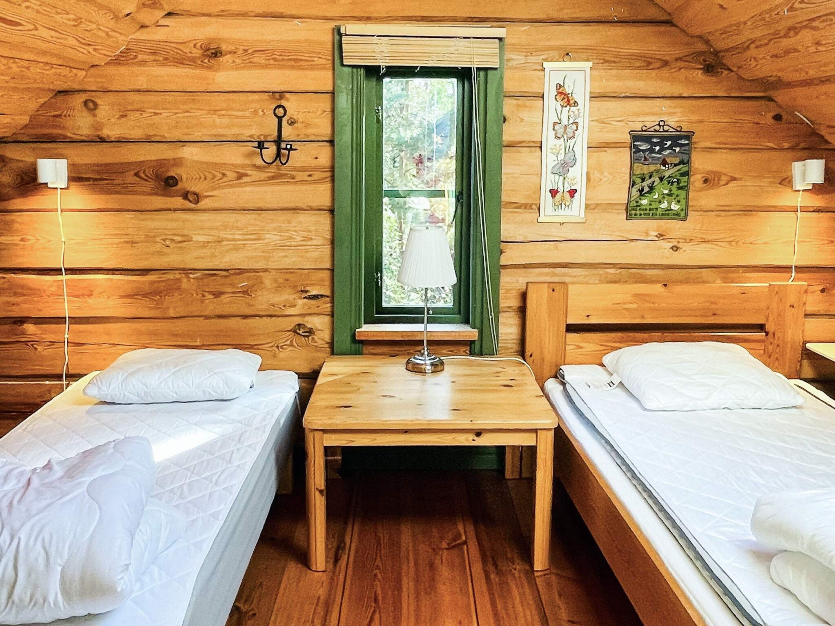 A cabin with two single beds, a small table, a window with curtains, and wall-mounted lights.