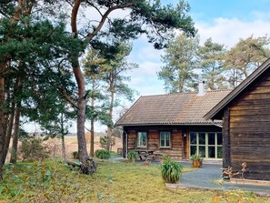 A rustic cabin with a tiled roof, surrounded by trees and a grassy area with a bench and potted plants. - 4 Star Holiday Home in Yngsjo (Yngsjo)