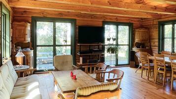 Interior de una cabaña de madera con comedor, sofá, televisión y cocina.