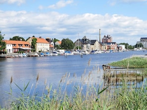 A riverside town with historic buildings, a marina with boats, and a calm water body.