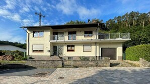 A two-story house with a balcony, a garage, and a paved driveway. - Holiday Apartment at Schillerfelsen (Dahn)