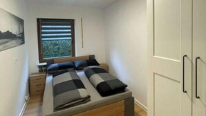 A bedroom with a bed, a window, a wardrobe, and a painting on the wall. - Holiday Apartment at Schillerfelsen (Dahn)