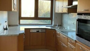 A kitchen with wooden cabinets, a built-in oven, and a window. - Holiday Apartment at Schillerfelsen (Dahn)