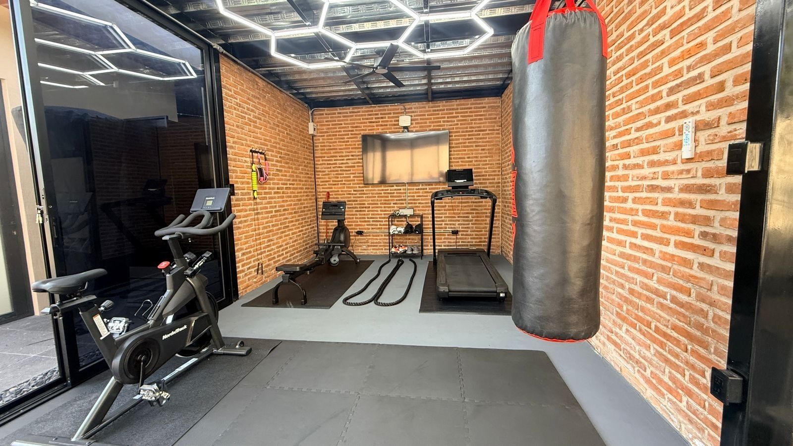 A gym with a stationary bike, treadmill, and punching bag.