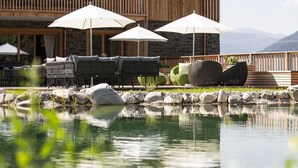 A pool with a wooden deck and outdoor seating, surrounded by rocks and greenery. - Spacious Chalet in Wolting With Sauna (Tamsweg)