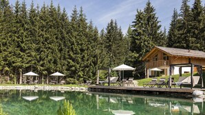 A clear pool with lounge chairs and umbrellas, surrounded by a wooden deck and a forested area. - Spacious Chalet in Wolting With Sauna (Tamsweg)