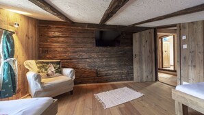 A rustic room with wooden walls, a single bed, a chair with a pillow, and a small rug.
