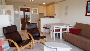 A living room with a brown leather sofa, two brown leather chairs, a white coffee table, and a dining table with red cushions. - Family Apartment in Nieuwpoort (Nieuwpoort)
