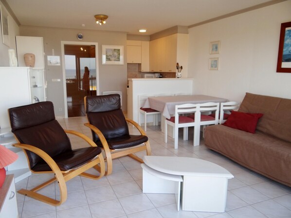 A living room with a brown leather sofa, two brown leather chairs, a white coffee table, and a dining table with red cushions. - Family Apartment in Nieuwpoort (Nieuwpoort)