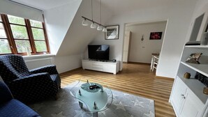Moderni olohuone, jossa on sohva, sohvapöytä, televisio ja kirjahylly.