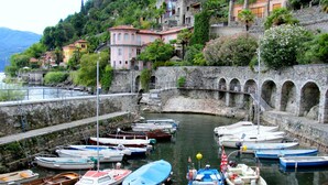 Un puerto deportivo con varias embarcaciones amarradas, muros de piedra y edificios en una colina.